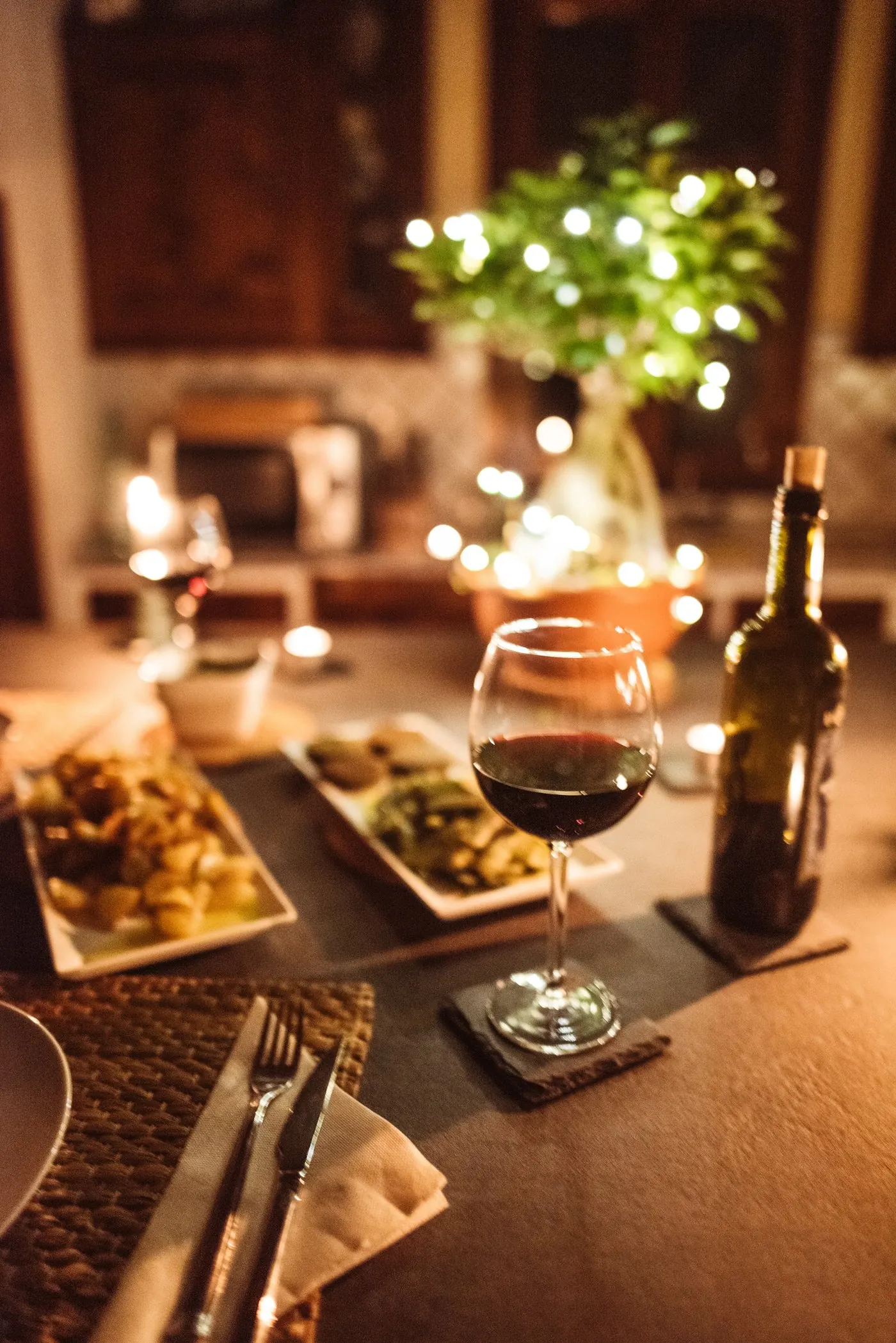 Candlelit table set for two with a glass of red wine and a warm dinner